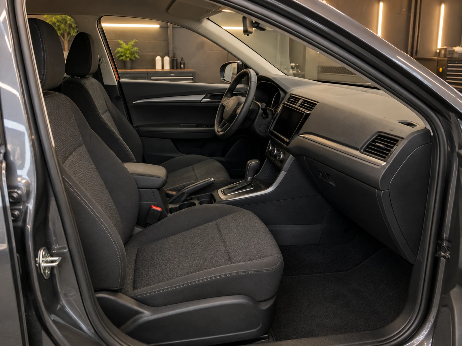 Interior de um carro com bancos, carpete e painel limpos, visto pela porta aberta.